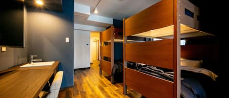 Quarto com beliche, uma escrivaninha de madeira e um banco, uma pia e um corredor que dá para outro quarto.