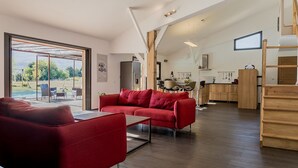 A spacious living area with a red sofa, a dining area with a kitchen in the background, and a large sliding glass door leading to an outdoor patio. - E case di u Puntale, Villa with swimming pool ideal for family vacations. (Ghisonaccia)