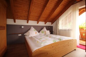 A wooden-framed bedroom with a bed, a nightstand, and a window with sheer curtains. - House Andrea B - House Andrea (Meersburg)