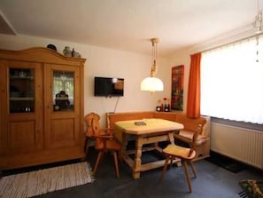 A dining area with a wooden table and chairs, a cabinet with glass doors, a television mounted on the wall, and a window with curtains. - House Andrea B - House Andrea (Meersburg)