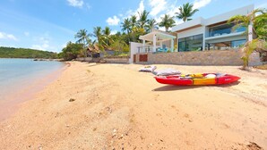 A beach with a red and yellow kayak, a modern house with large windows, and palm trees. - Modern Beachfront Villa near Fishermans Village (Bophut)