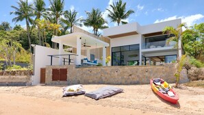A modern house with a covered patio, a stone wall, and a red kayak on the sand. - Modern Beachfront Villa near Fishermans Village (Bophut)