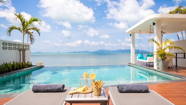 A poolside area with lounge chairs, a table with a basket of fruits and a glass of water, and a view of the sea and mountains. - Modern Beachfront Villa near Fishermans Village (Bophut)