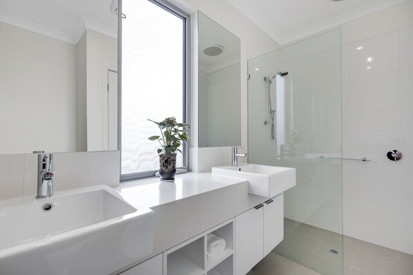 Une salle de bain moderne avec une grande fenêtre, un lavabo blanc, un miroir et une douche en verre.