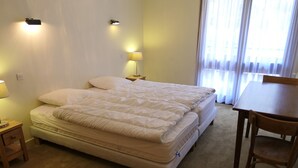 A bedroom with a bed, bedside lamps, a wooden nightstand, a wooden chair, and a window with curtains.