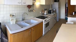 A compact kitchen with white cabinets, a double sink, a stove, and a washing machine.