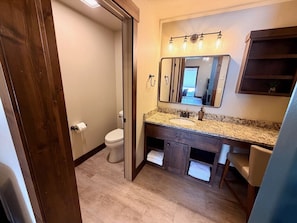 A bathroom with a toilet, sink, mirror, and wooden cabinet.