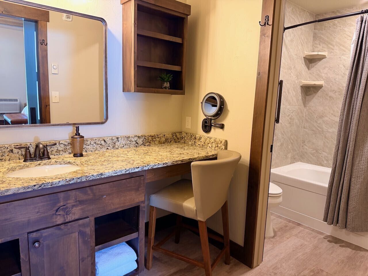 Une salle de bain avec un lavabo sur un plan de travail en granit, un meuble-lavabo en bois, un miroir, une douche avec une porte en verre et des toilettes.