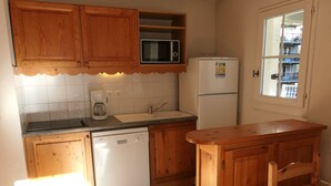 A kitchen with wooden cabinets, a microwave, a refrigerator, a dishwasher, a sink, and a window with a view of a balcony.