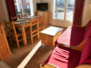 A cozy room with a wooden dining table set for four, a TV on a stand, and a red sofa.