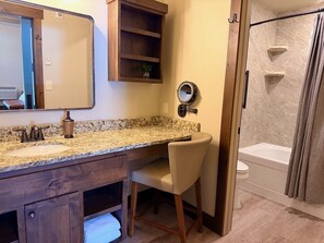 Un baño con lavamanos de encimera de granito, tocador de madera, un espejo, ducha con puerta de cristal y un inodoro.