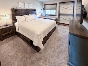 A bedroom with a large bed, a nightstand, a lamp, a window with a view, and a wardrobe.