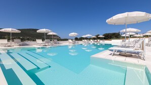 Ein klares, blaues Schwimmbecken mit weißen Sonnenschirmen und Liegestühlen, umgeben von einer weißen Poolterrasse.