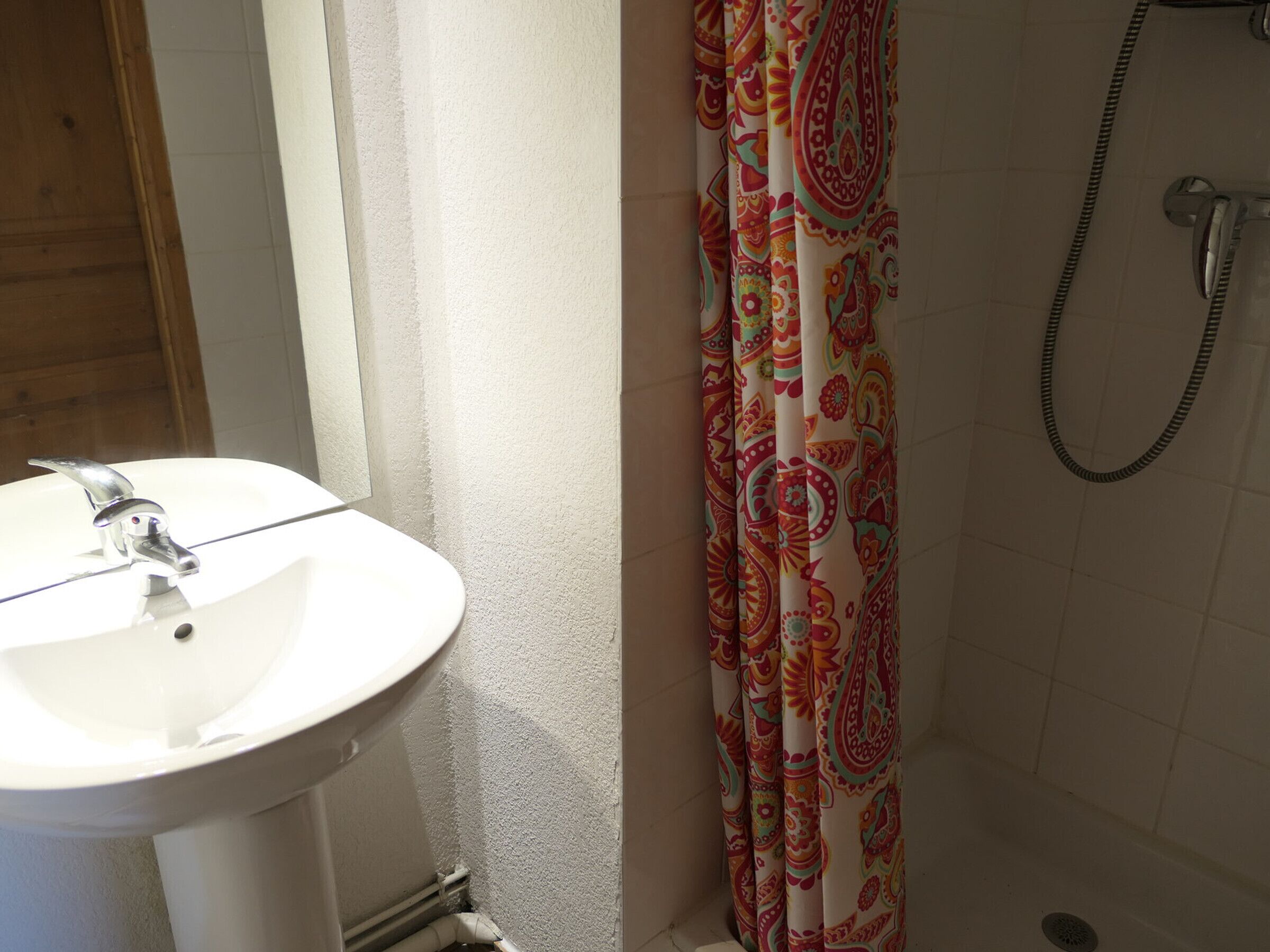 Une salle de bain avec un lavabo blanc, un rideau de douche à motifs cachemire et une pomme de douche.
