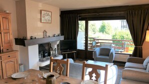 Un coin repas avec une table en bois dressée pour quatre personnes, un téléviseur et une cheminée.