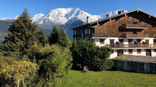 Un chalet avec une façade en bois, un balcon et une vue sur des montagnes enneigées.