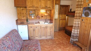 Une cuisine de taille réduite, dotée de meubles en bois, d’un petit réfrigérateur et d’un canapé à motifs.