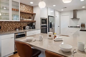 Una cocina moderna con armarios blancos, horno empotrado, refrigerador y un comedor con mesa y sillas.
