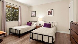 Een kamer met twee eenpersoonsbedden, een nachtkastje met een lamp, een houten dressoir en een raam met gordijnen.