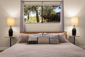 A bedroom with a bed, two bedside lamps, a window with a view of trees, and a patterned pillow. - The Great Escape! Modern, Secluded Retreat, Views! (Sedona)