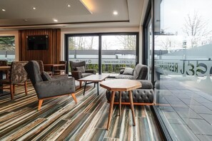 Un área de estar moderna con una variedad de opciones de asientos, incluyendo sofás y sillones, y una mesa de centro de madera. Ventanas amplias ofrecen vistas al exterior.