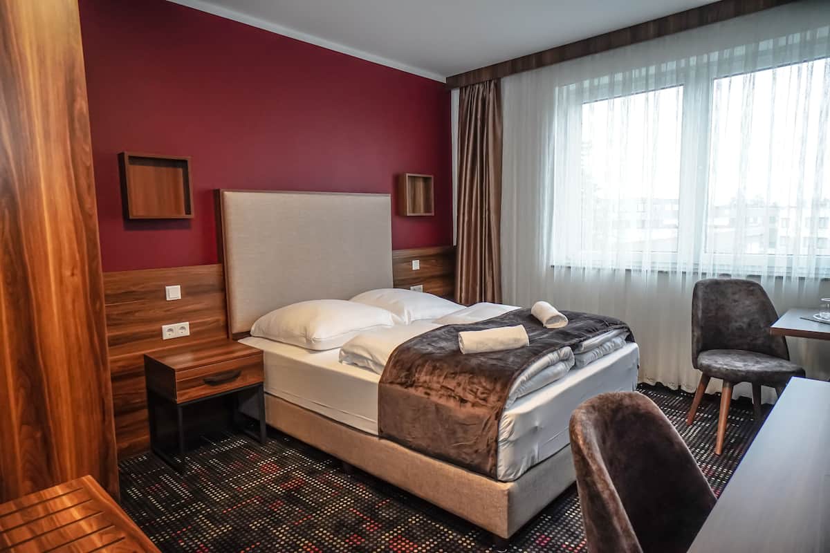 A hotel room with a bed, a desk, a chair, and a window with curtains.