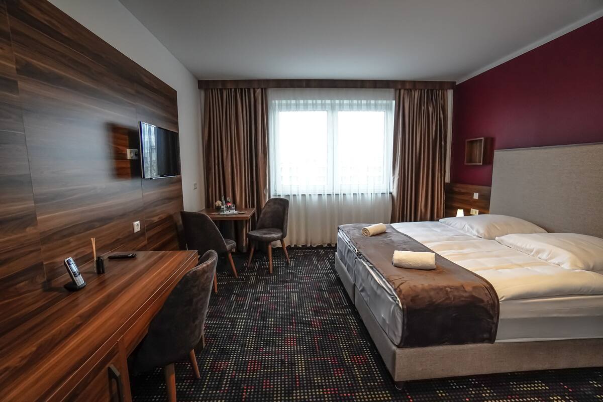 A hotel room with a bed, desk, chair, and a TV mounted on the wall.