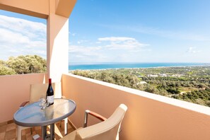 Ein Balkon mit Tisch und Stühlen, einer Weinflasche und Blick auf das Meer und die Landschaft.