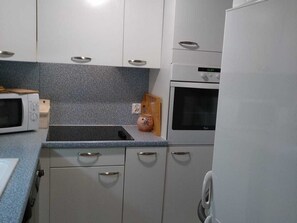 Cozinha com armários brancos, micro-ondas, torradeira, pia e geladeira.