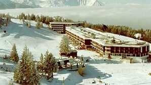 Un hôtel enneigé composé de plusieurs bâtiments, entouré d’arbres et avec des montagnes en toile de fond.