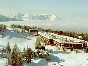Um hotel coberto de neve com vários edifícios, rodeado por árvores e montanhas ao fundo.