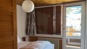 Une chambre avec un lit, un radiateur, un plafond en bois et une porte-fenêtre coulissante donnant sur un espace extérieur.