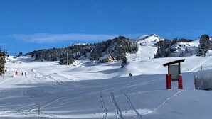 Une piste de ski enneigée, avec un chalet, un télésiège et un petit bâtiment doté d’un toit rouge.