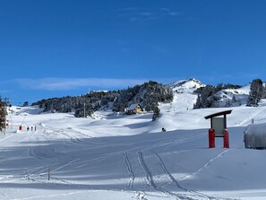 Pista de esqui coberta de neve com uma hospedaria, teleférico e um pequeno edifício com telhado vermelho.