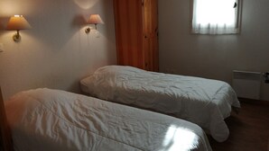 Habitación con dos camas, armario de madera, lámparas de pared y ventana con cortinas.