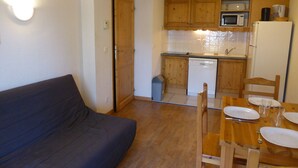 Un espacio habitable compacto con sofá, mesa de comedor para dos personas, armarios de madera, microondas y lavavajillas.