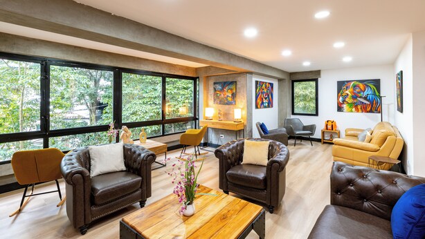 A spacious living area with leather sofas, a wooden coffee table, and large windows offering a view of greenery. - Serene Escape in Provenza (Medellin)