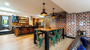A modern kitchen with a brick wall, wooden flooring, and a dining area with green chairs. - Serene Escape in Provenza (Medellin)