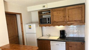 A compact kitchen with wooden cabinets, a white refrigerator, a microwave, a Bosch dishwasher, and a coffee maker.