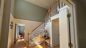 A spacious hallway with wooden flooring, a staircase with white railings, and a chandelier. - Family Waves with beach on Lake Winnipesaukee! (Meredith)