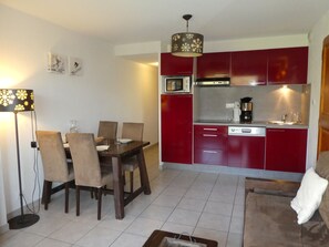 A compact kitchen with red cabinets, a microwave, and a coffee maker. There is a dining table with chairs and a floor lamp.