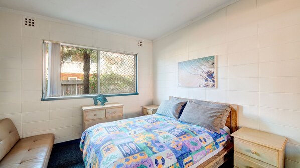 A bedroom with a bed, a dresser, a nightstand, a window, and a painting on the wall. - Forster Holiday Lodge 03 (Forster)