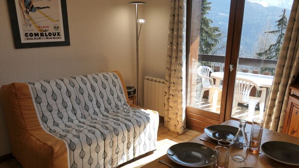 Una sala de estar amoblada con sofá, mesa de comedor para dos personas y vista a las montañas a través de un ventanal.