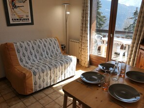 A furnished living room with a sofa, dining table set for two, and a view of mountains through a glass door. - Studio for 4 with balcony near shuttle (Saint-Gervais-les-Bains)