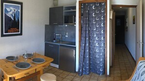 Cocina compacta con mesa de comedor y taburetes, kitchenette, sofá y cortina de ducha con estampado de hojas.