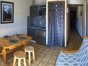 A compact kitchen with a dining table and stools, a kitchenette, a sofa, and a shower curtain with a leaf pattern.