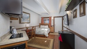 Ein kleines Hotelzimmer mit Küchenzeile, einem Bett, einem Fernseher und einer kleinen Essecke.