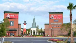 L’entrée d’un centre commercial, avec des enseignes TangerOutlet, un phare et un magasin Banana Republic.