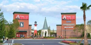 Entrada a un centro comercial con pancartas de Tanger Outlet, un faro y una tienda Banana Republic.