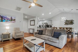 A spacious living room with a ceiling fan, a sofa, a coffee table, and a painting of a mountain landscape.